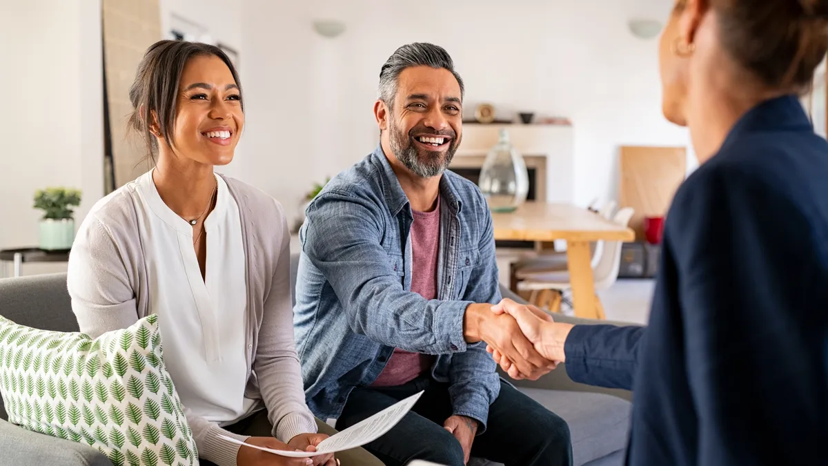 Happy smiling couple greeting broker with handshake at home.