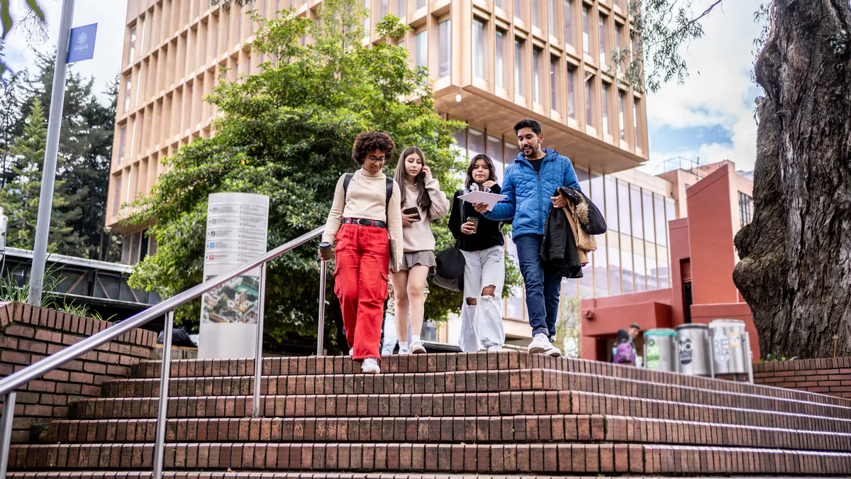 A group of college students chats while walking down stairs on campus.