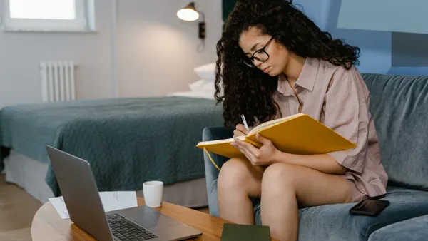A young woman writes in a notebook on the couch