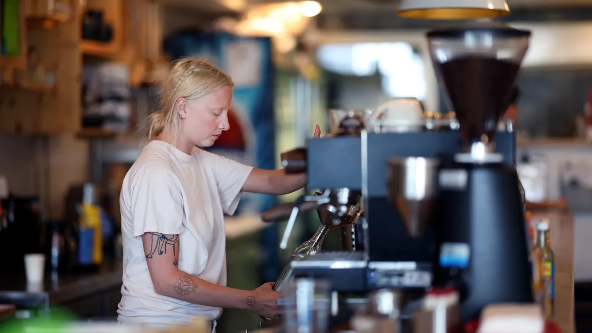 A person in a white t-shirt works behind the counter at a cafe.