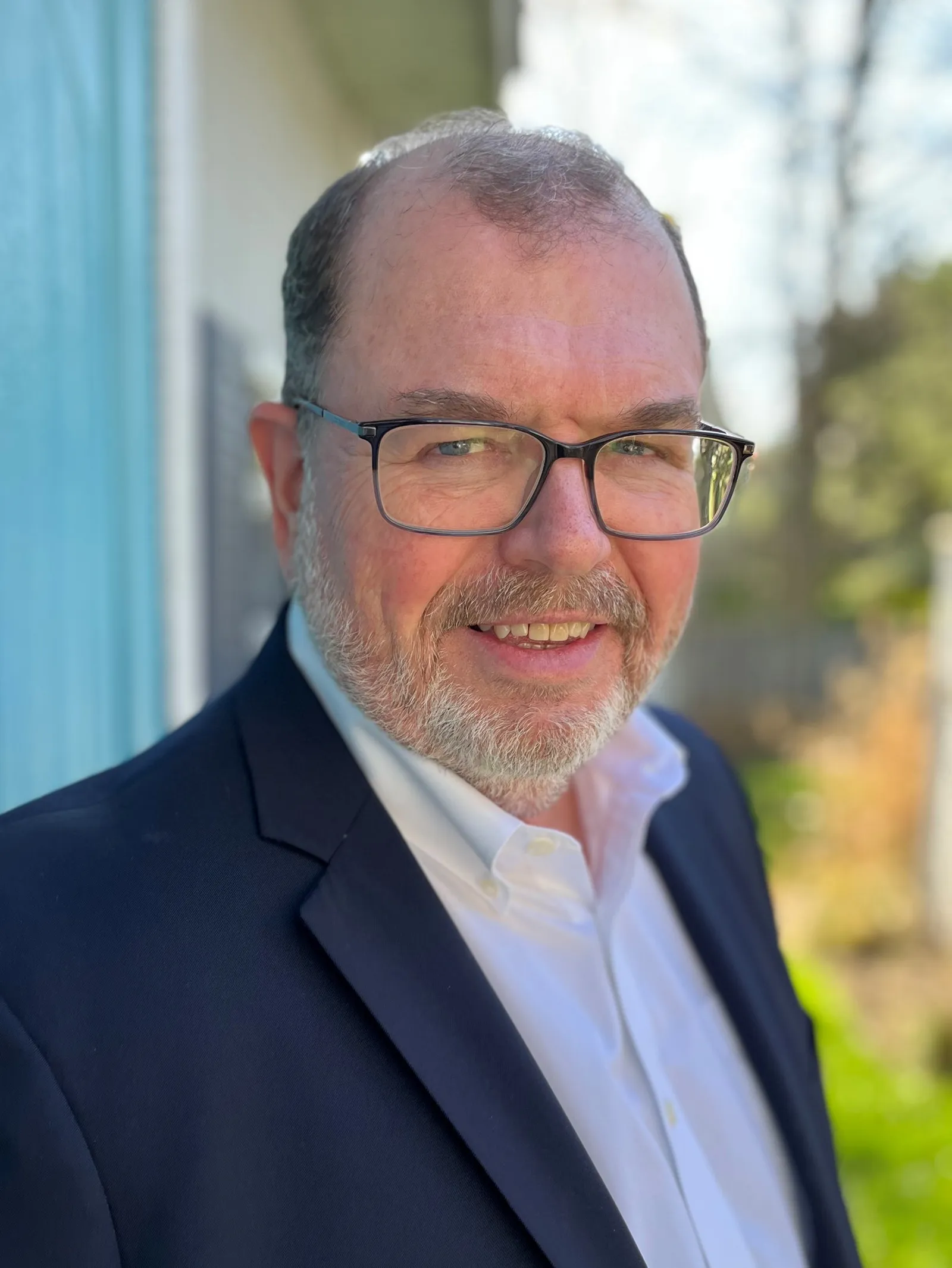 Man with blue blazer and white shirt smiling at camera.