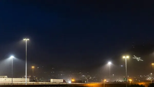 A truck travels on a highway lit up by lights at night.