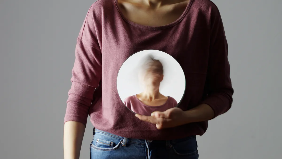 A faceless person holds a mirror, with the back of their head reflected