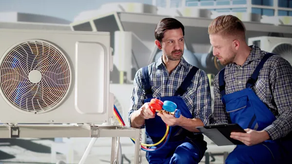 An HVAC technician shows another worker readings from a cooling system.