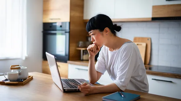 Customer looks at laptop computer with a credit card in hand looking concerned.