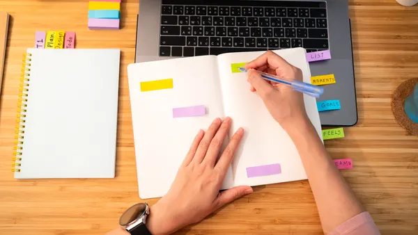 Bird's eye view of hands writing on a calendar on top of a laptop sitting on a table