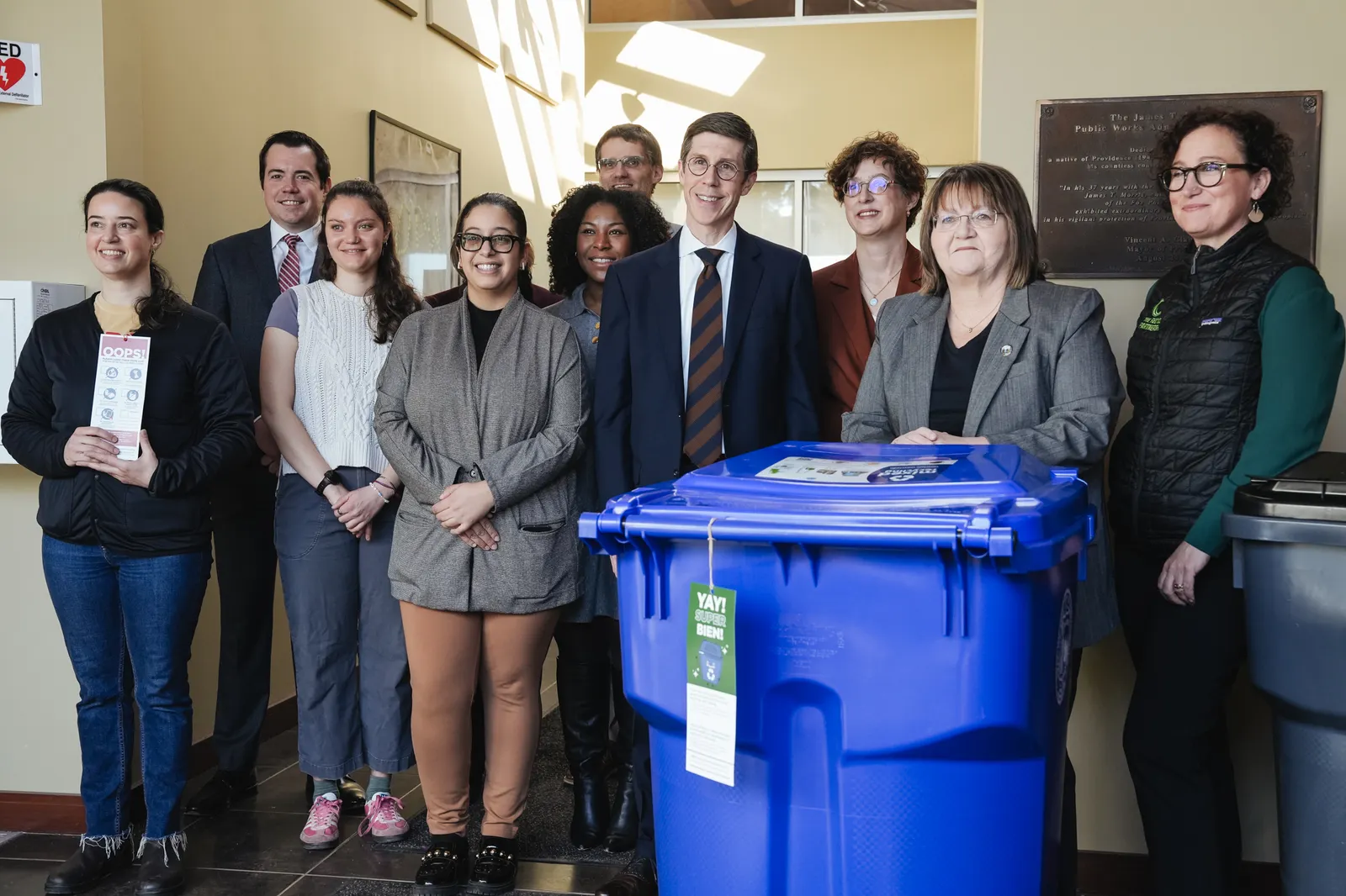A group of people stand in front of a new blue recycling cart in Providence, Rhode Island