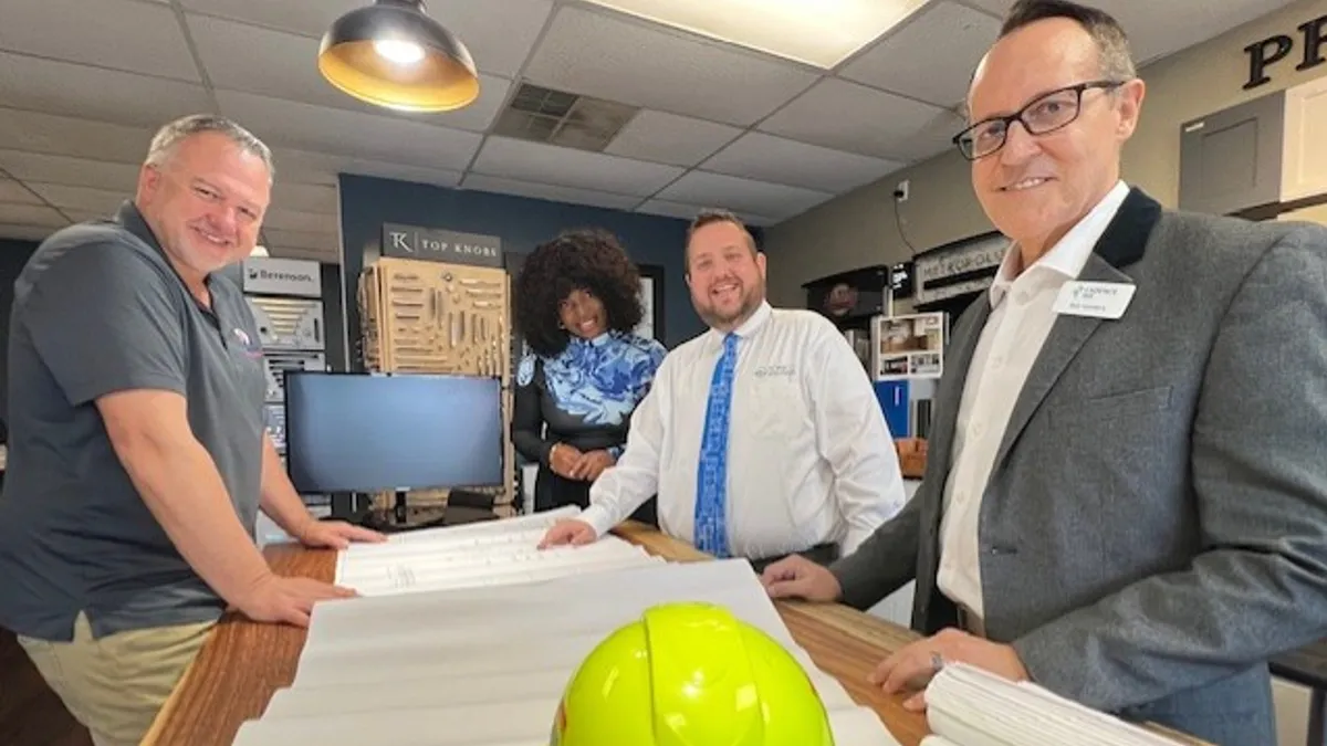 Four people stand around a table with a hard hat and construction drawings.