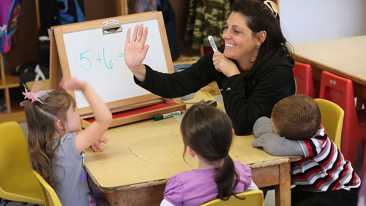 An adult sits at a table with young children. The adult high 5s one child