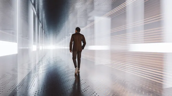 A man in a brown suit is walking down a futuristic glass and metal corridor