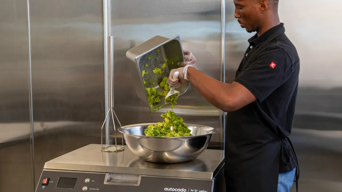 A man in a Chipotle uniform removes processed avocado from tray.