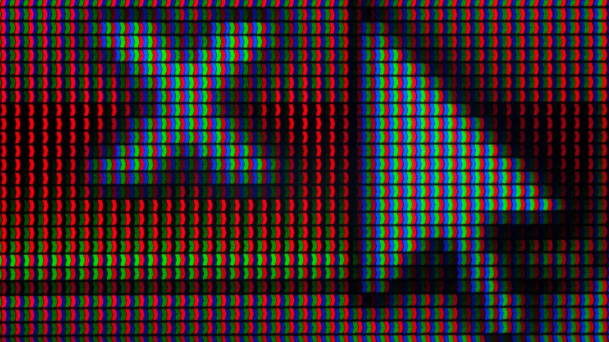 A close up of a cursor arrow hovering over an X on a screen, pixelated with red, blue and green colors.