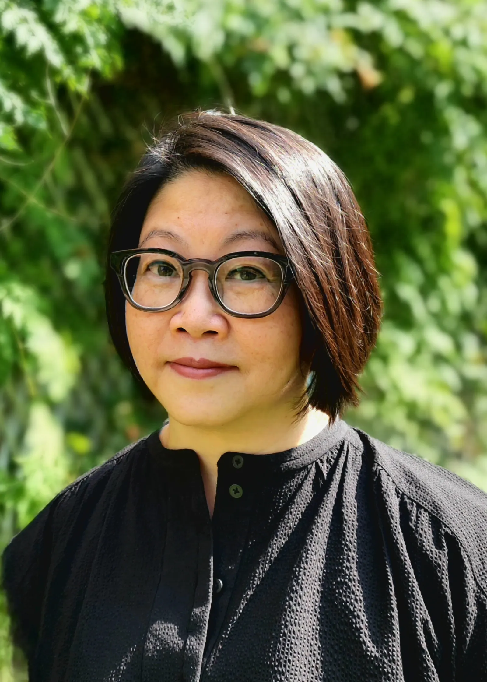 A smiling woman in a dark outfit in front of a green background.