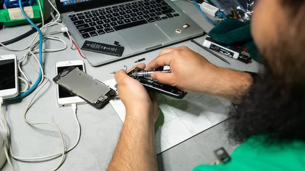 A close-up of an employee using tools to repair a cell phone in a warehouse.