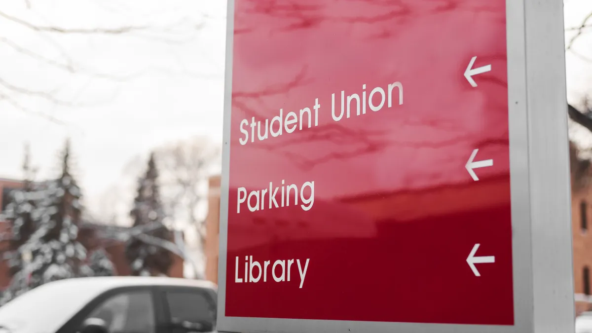 Red sign at university campus showing directions to student union, parking spaces and library.