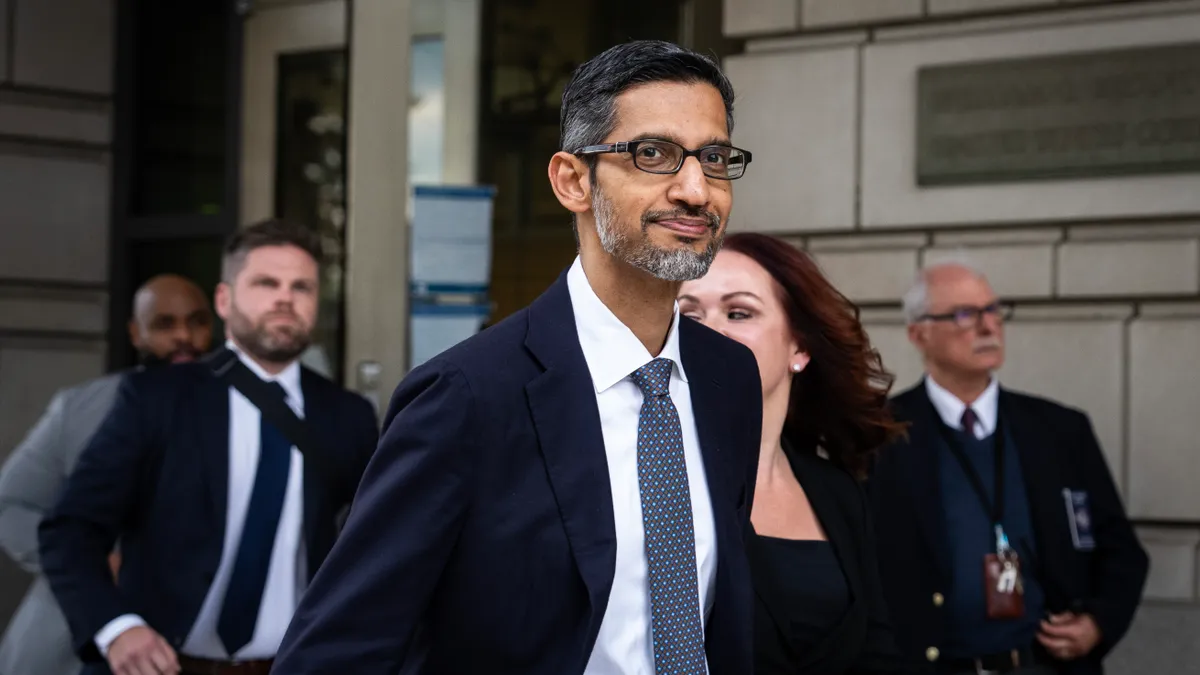 A man in a navy blazer and gray tie walking out of a gray brick building