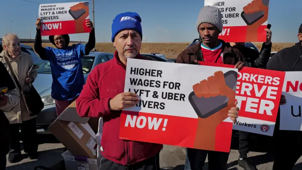 People outdoors holding signs reading "Higher wages for Lyft & Uber drivers now!"