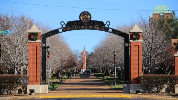 University sign above a gate leading to campus with people walking in the background.