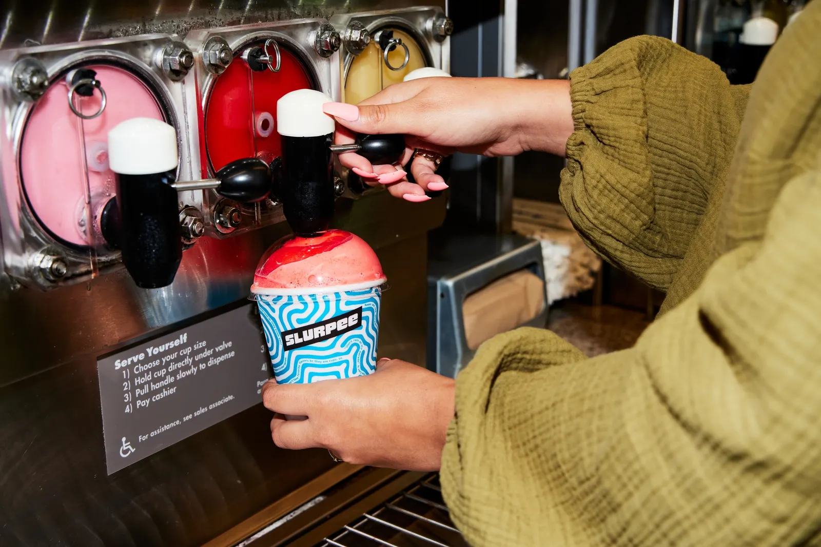 A photo of a person dispensing a Slurpee at a 7-Eleven store.