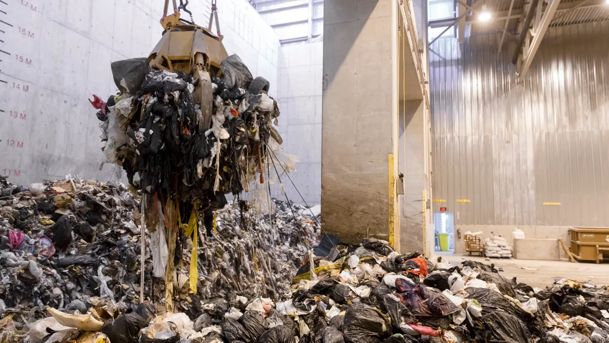 Mechanical claw hovering over pile of trash in industrial facility