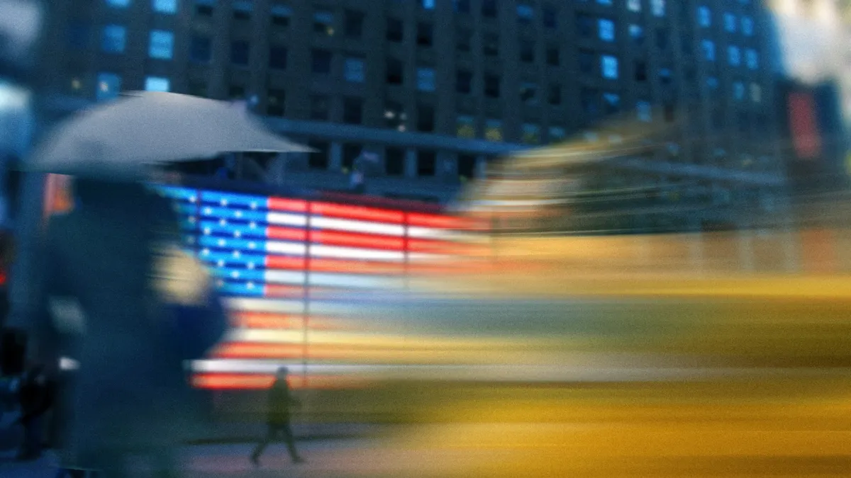 A blurred view of a city street, neon U.S. flag and person with an umbrella.