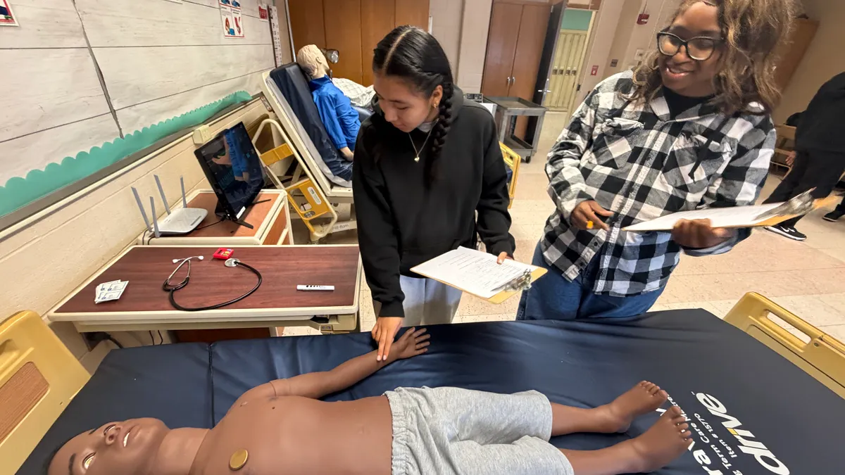 Two students work with an artificial intelligence-enabled mannequin in a healthcare career education program.