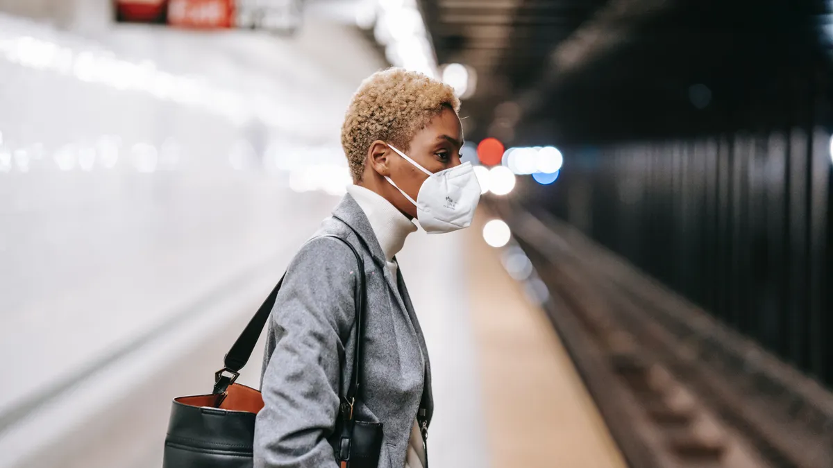 A masked Black person waits for public transportation