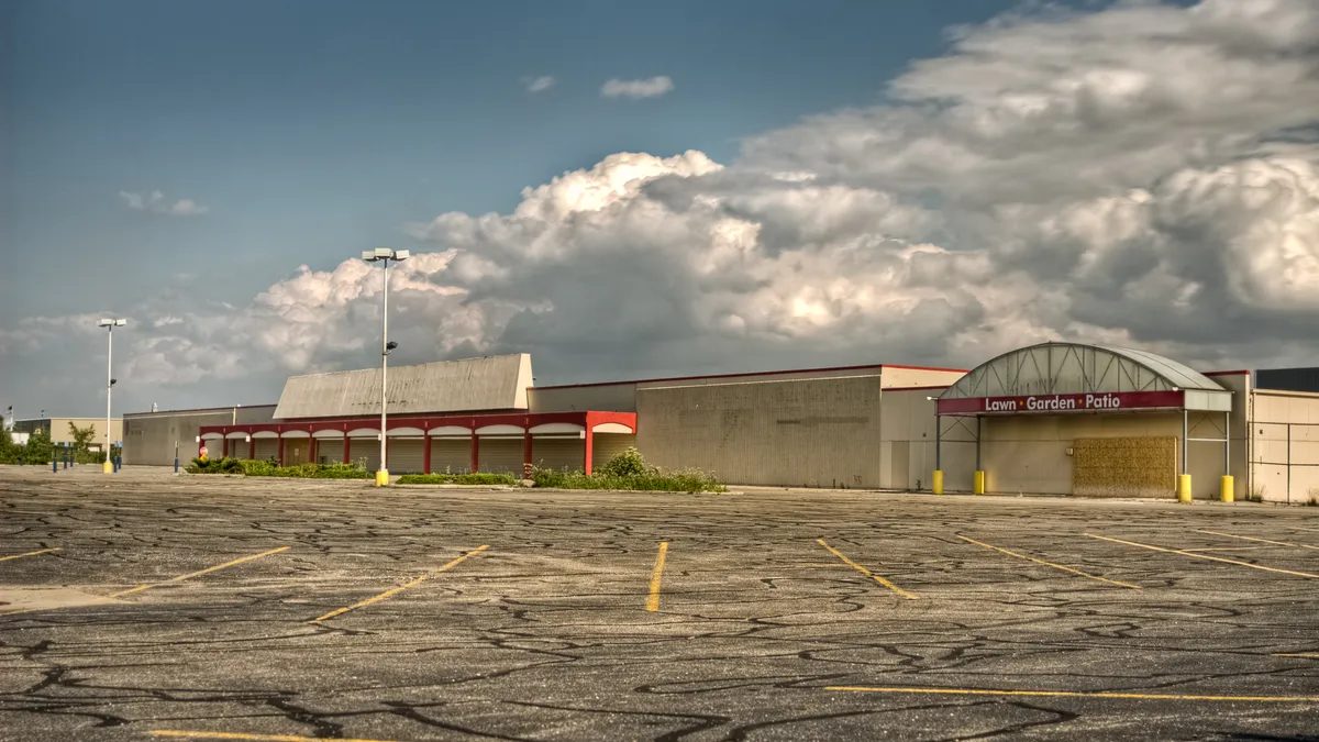 An empty, vacant commercial store with overgrown weeds and empty parking lot in the foreground.