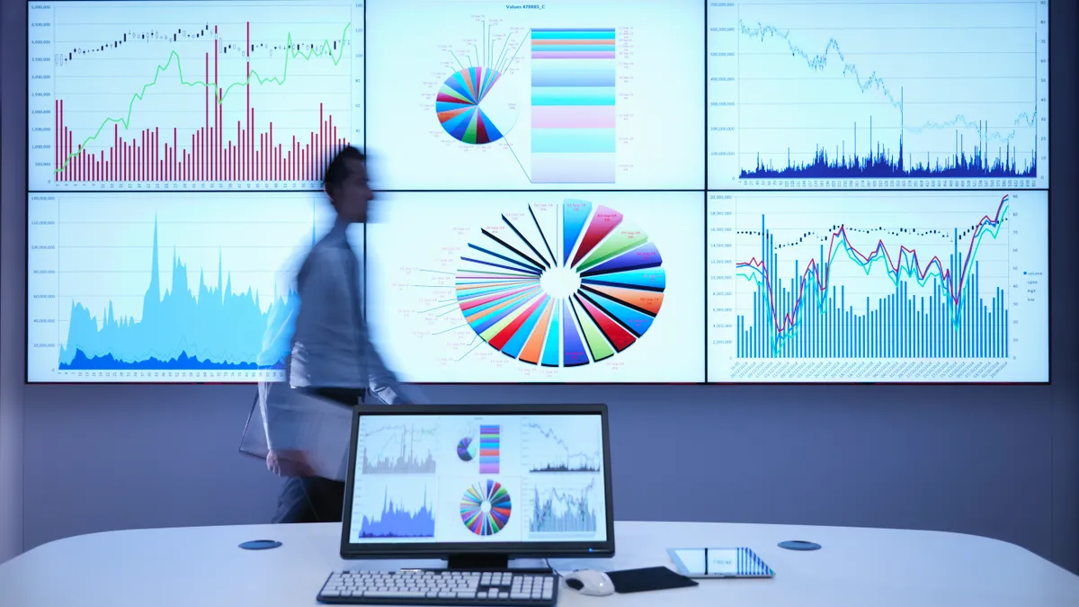 Businessman walking in front of graphs on screen