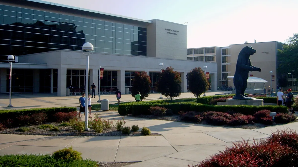 A massive bronze bear statue stands in front of a campus building on a nice, sunny day.