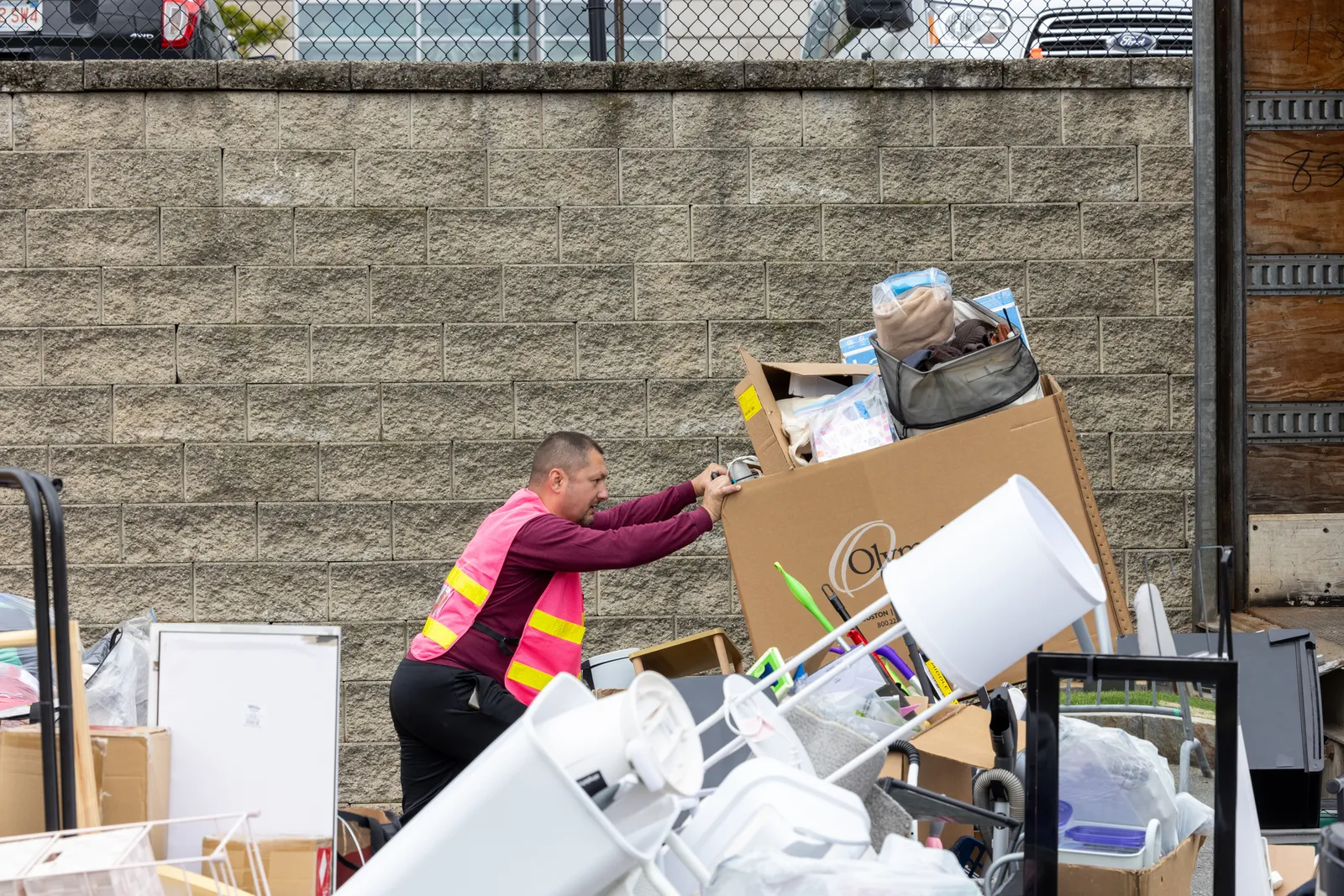 A person in a safety vest pushes a bin of items to be donated onto the back of a large truck.