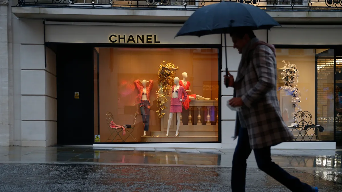 A person with an umbrella walks in front of a Chanel store.