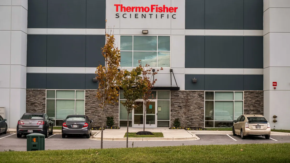 Exterior of a modern Thermo Fisher Scientific building featuring a prominent sign above a glass entrance, with cars parked in front.