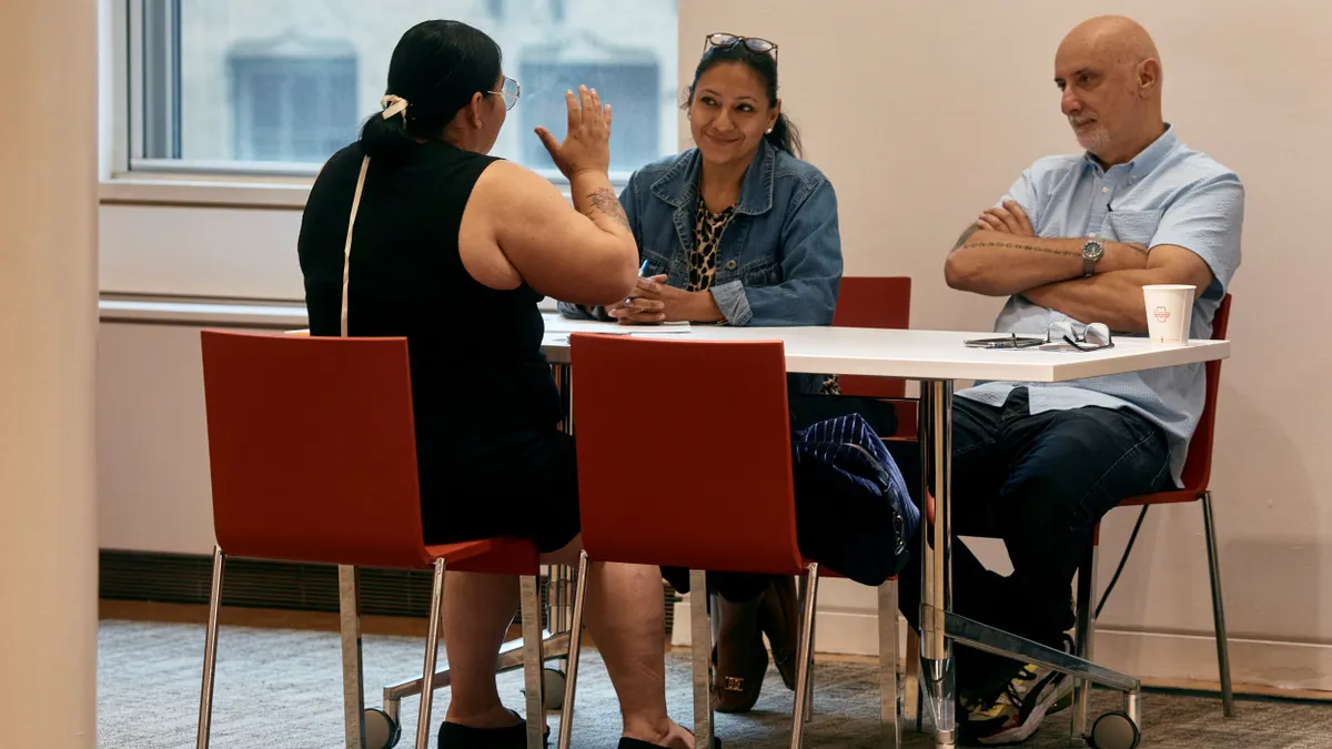 An individual engaged in conversation sits at a table across from two others.