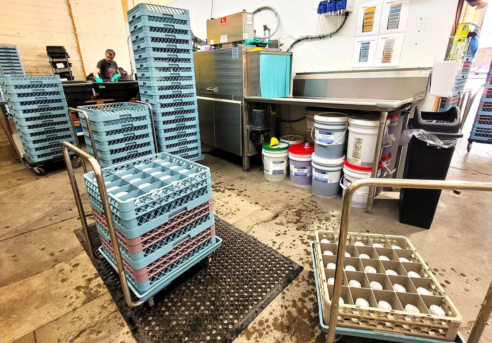 People work in an industrial washing facility while stacks of cleaned foodservice ware are nearby.