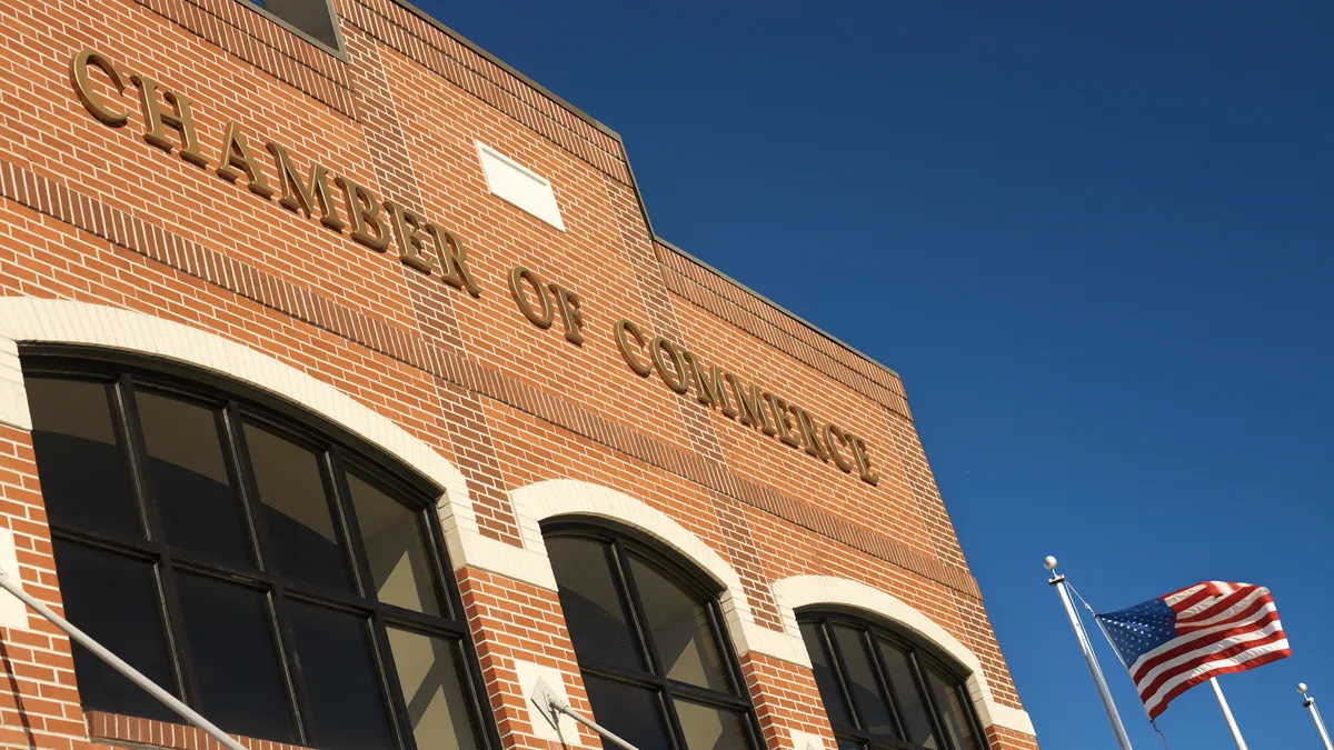 Top half of a Generic small town brick building with Chamber of Commerce in raised brass lettering on front facade. American Flag flying.