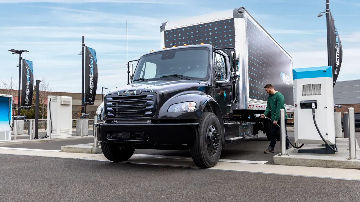 A driver charges a Freightliner eM2 medium duty battery-electric truck.