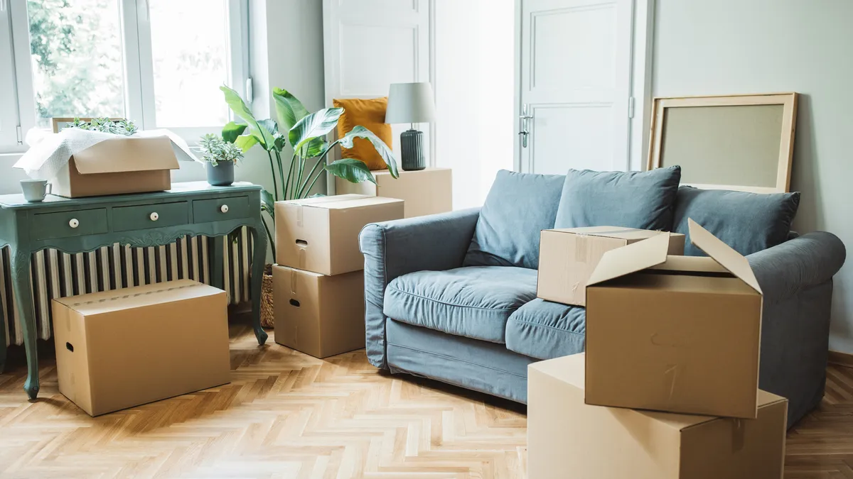 A room with a blue couch, covered in cardboard boxes.