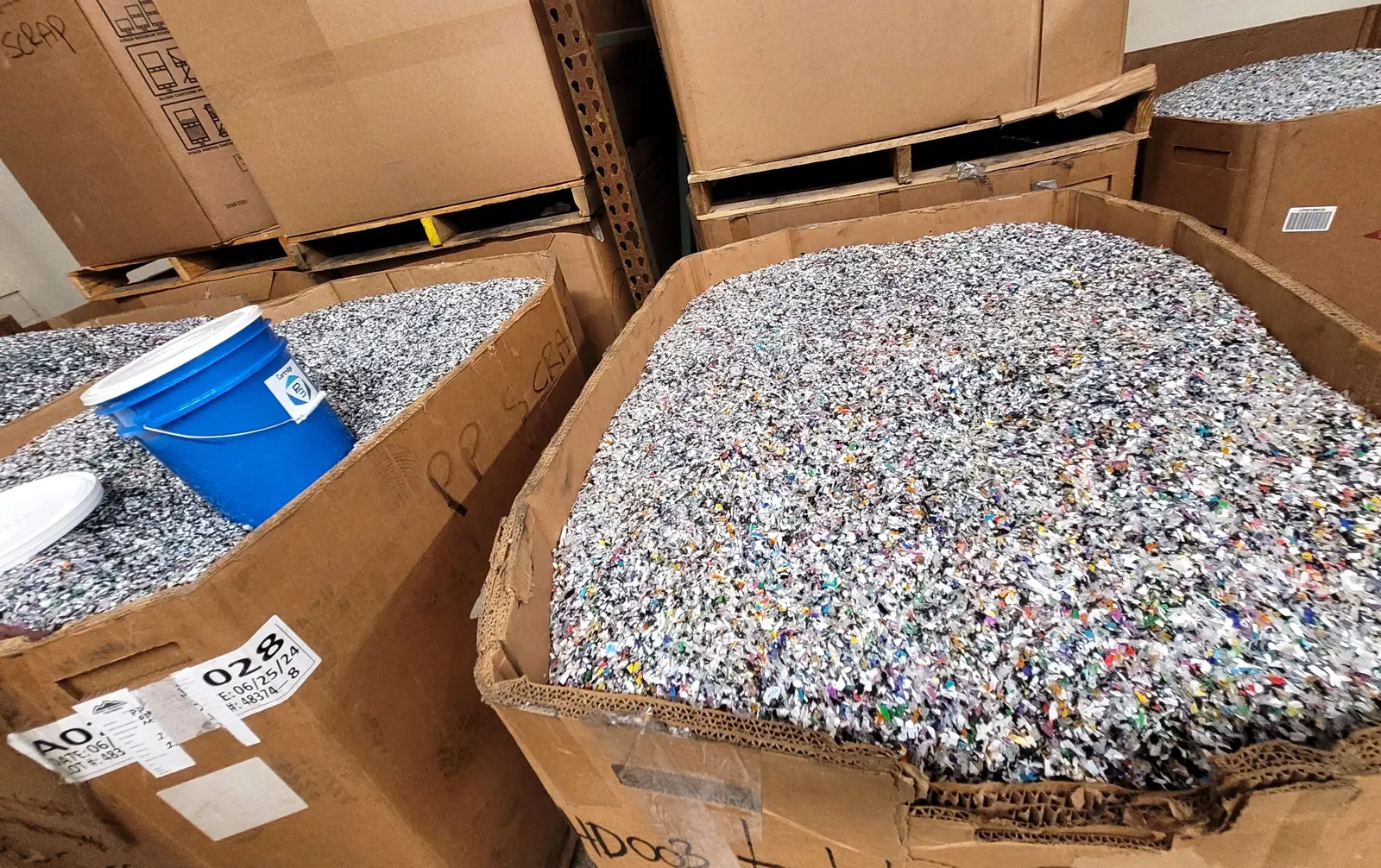 A close-up shot of large industrial boxes filled with multicolored plastic flakes.