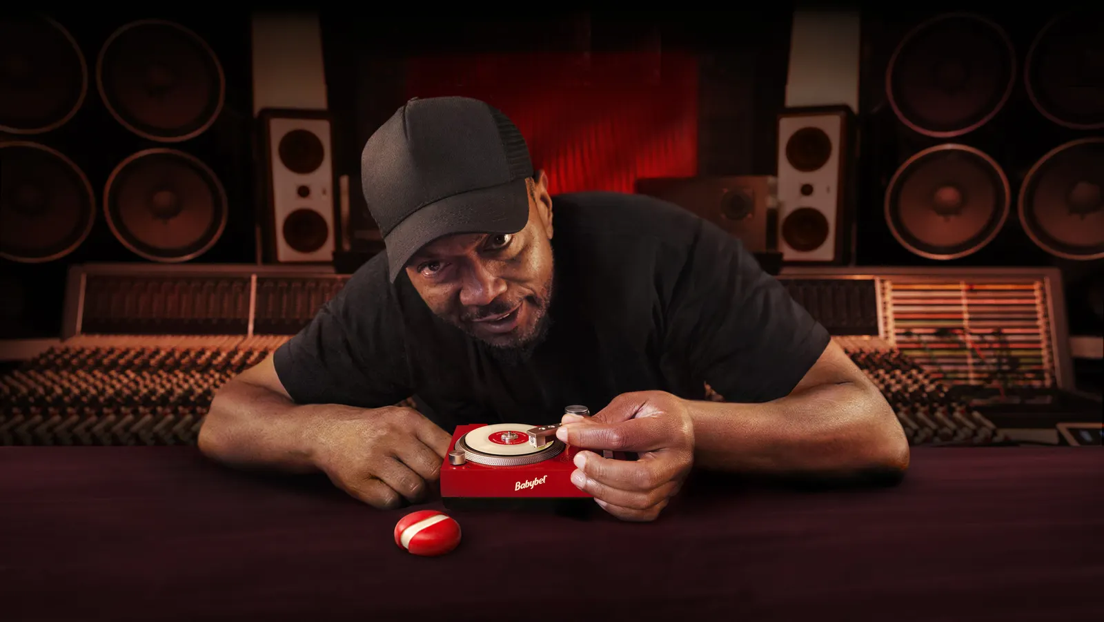 Musician Timbaland wearing a hat and playing a small vinyl record on a red turntable