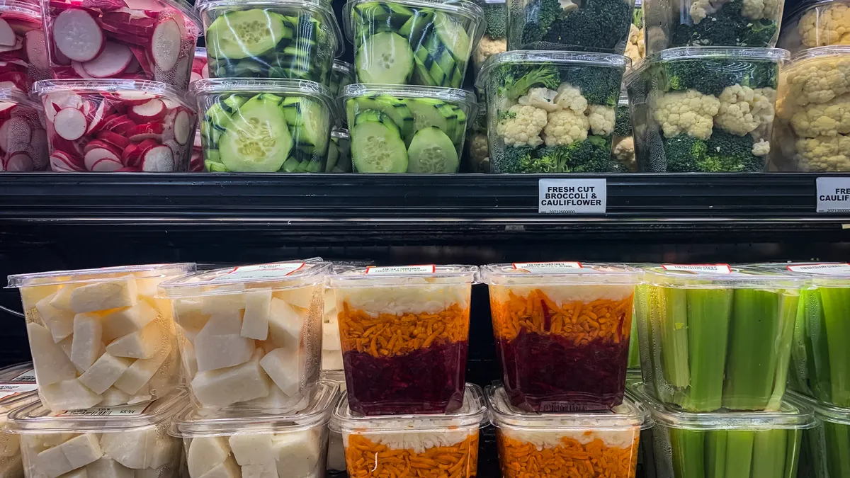 Shelves of stacked plastic containers containing freshly cut veggies, on display at grocery store