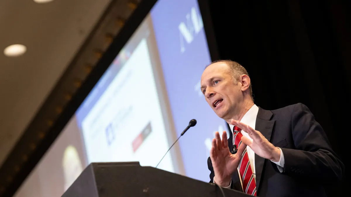 Chicago Federal Reserve President Austan Goolsbee stands at podium with hands up and lighted screen behind.