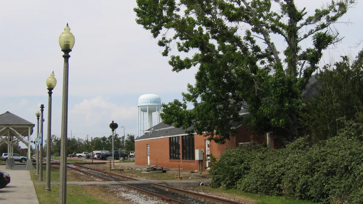 A red brick building alongside a railroad track and a station platform on the opposite side and a water tank label "Gulfport" in the background.