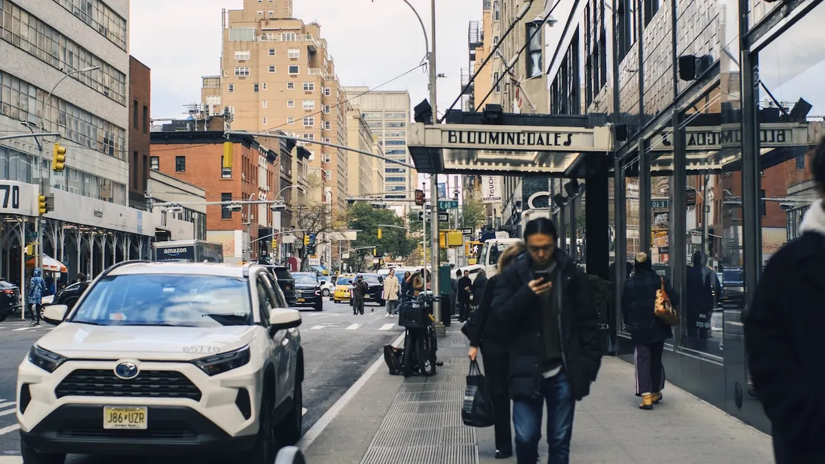 People walking down the street and cars driving in a city.