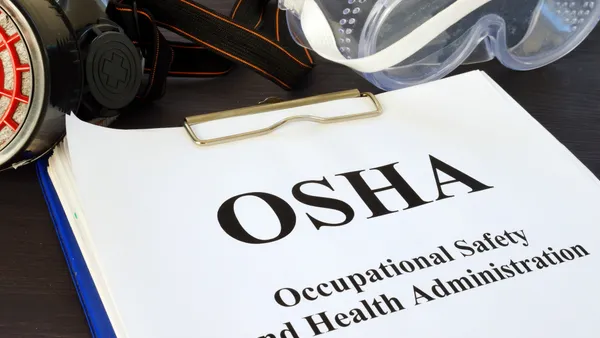 A blue clipboard with a white paper that says "OSHA, Occupational Safety and Health Administration," and protective gear lying above it.