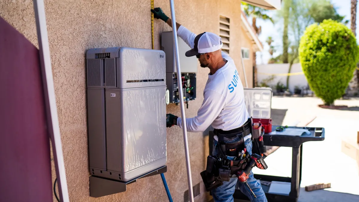 A worker uses a tape measure next to electrical boxes installed on a home.