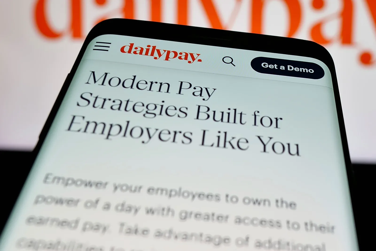 A hand holds a smartphone displaying the DailyPay website.