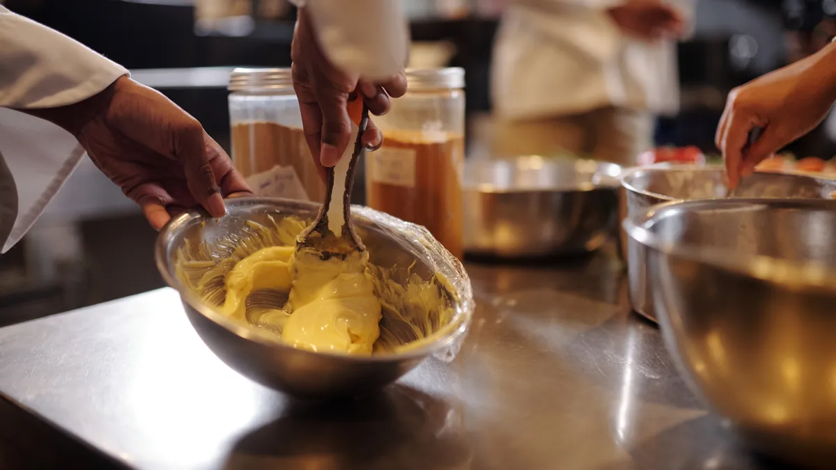 Closeup image of cook beating dairy butter and salt in metal bowl