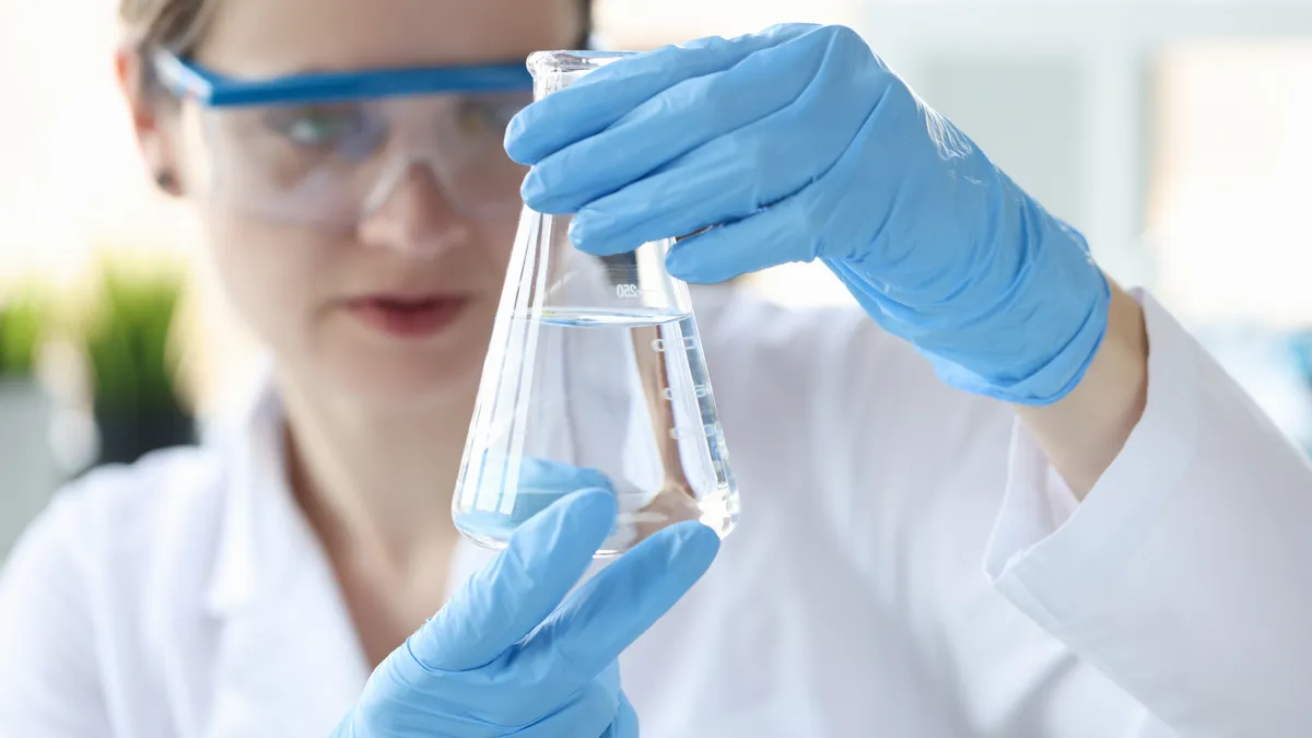 Woman scientist holding flask with transparent liquid in her hands closeup. Checking water quality and ph concept.