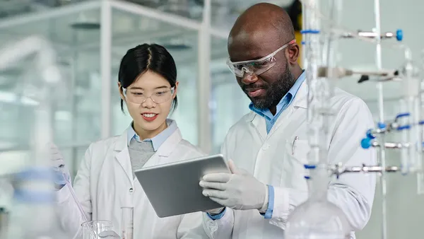 Two scientists in lab collaborating on a tablet.